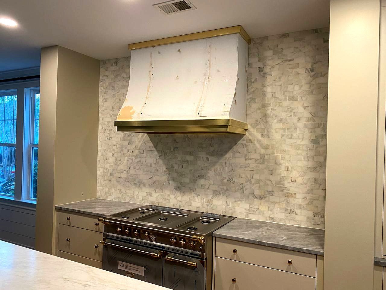 Curved range hood with brass trim bands, prepped for paint, over a French range and marble tile