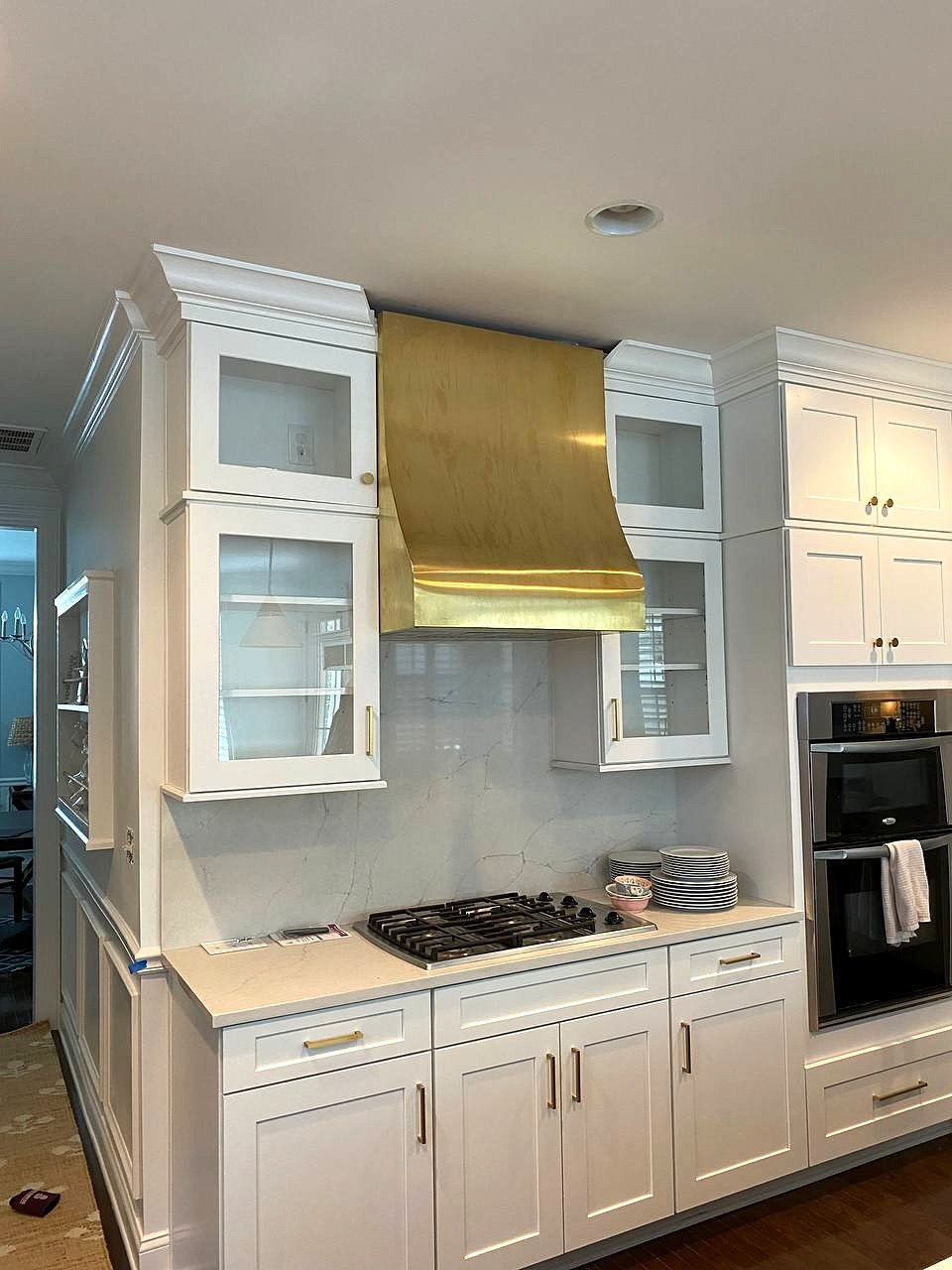 Curved brass range hood between glass-front wall cabinets over a gas cooktop
